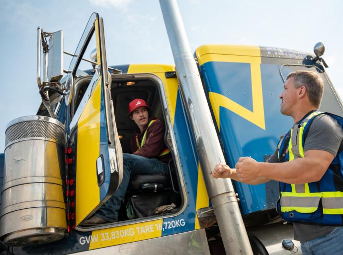 Student sitting in the cab of a semi-truck receiving instruction from a driving instructor