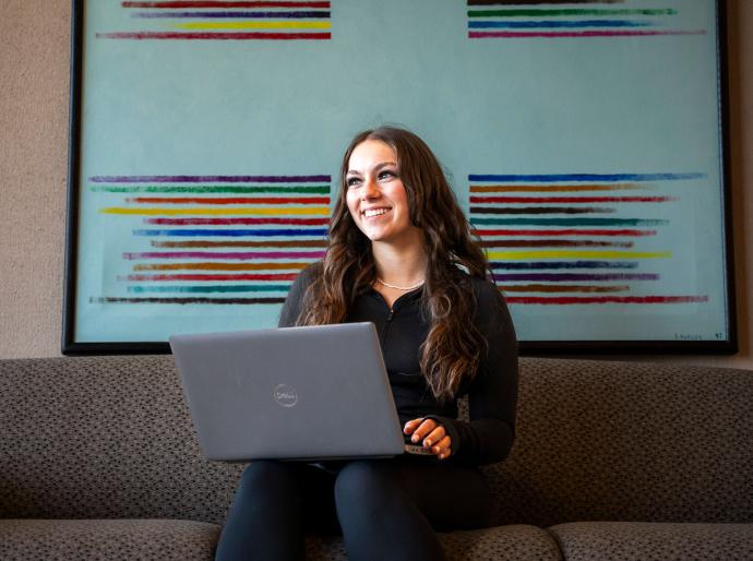 Student with a laptop sitting on a couch with a colourful painting in the background