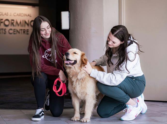 2 students petting a therapy dog on the theatre concourse in the Cardinal building on Grande Prairie Campus