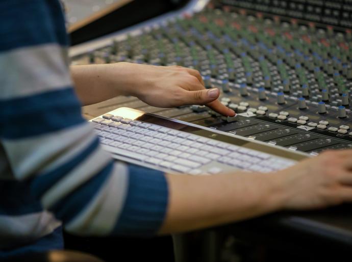  A person adjusting sliders on a mixing deck in a recording studio.