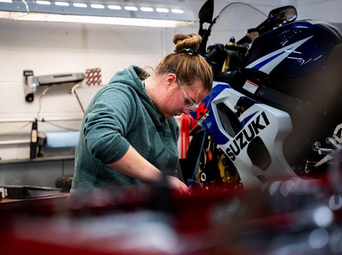 An NWP student focused on repairing a motorcycle in a well equipped workshop.