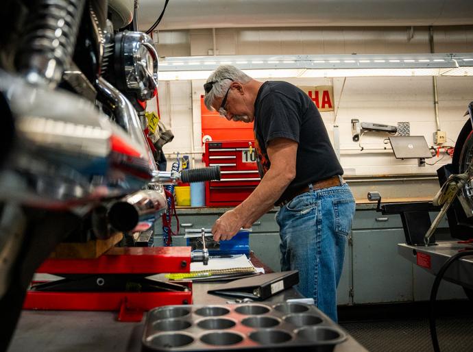 An NWP motorcycle mechanic instructor focused on repairing a motorcycle in a well-equipped workshop, surrounded by tools and parts