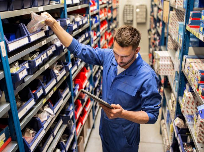 Parts technician reading a list off a clipboard and reaching into a bin of parts