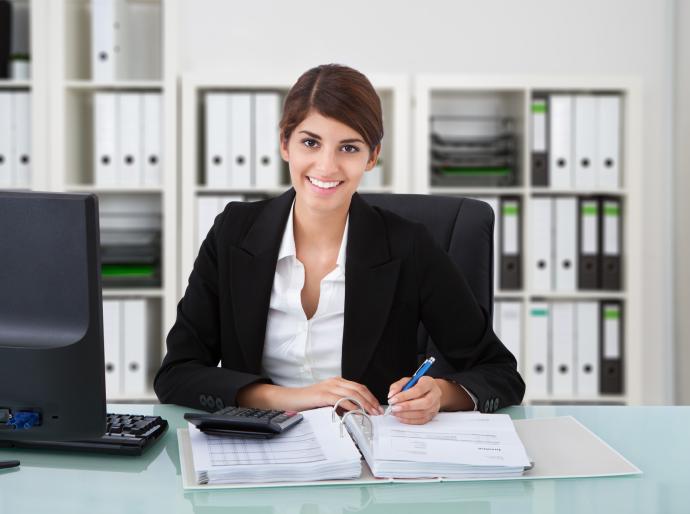 A smartly dressed professional woman smiling at her desk while working.