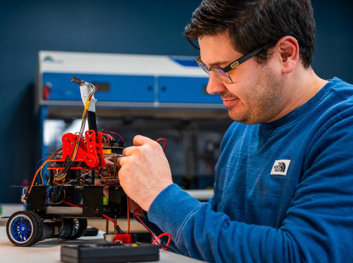 A computing science student working intently on a robotic gadget in the lab.