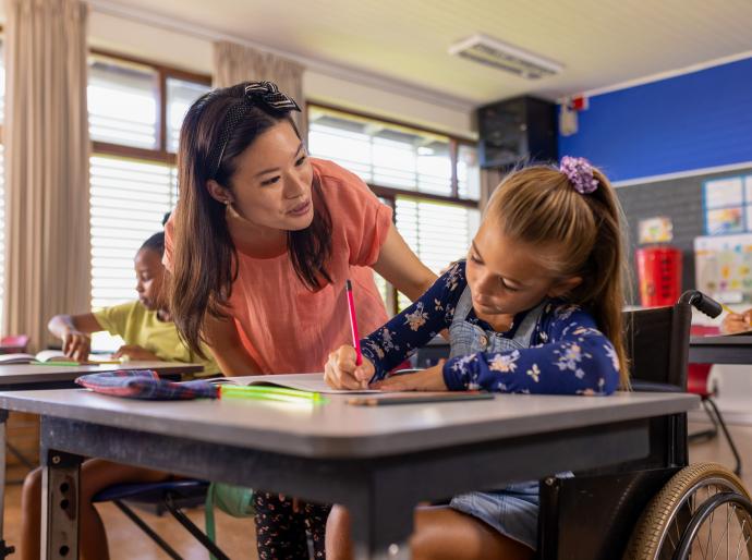 An educational assistant helping a student in a wheelchair with her writing assignment