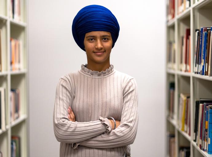 An intelligent looking woman with a blue head scarf standing in-between book shelves in a library
