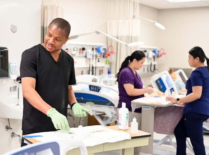 Group of nursing students with gloves on their hands and wearing scrubs working in the simulation lab