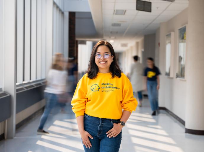 Happy student standing in a hallway on GP campus wearing a bright yellow sweatshirt 
