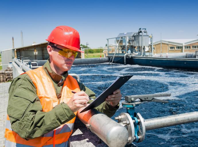 A technician with a clipboard monitoring the quality of water at a waste water treatment plant.