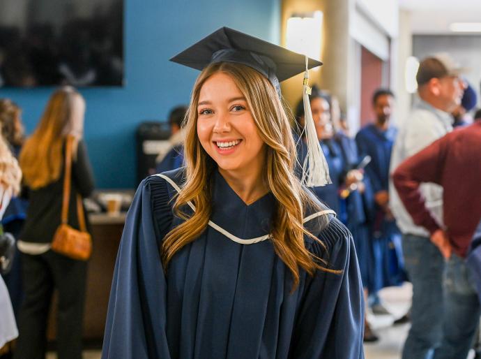 A happy graduate dressed in cap and gown smiling broadly