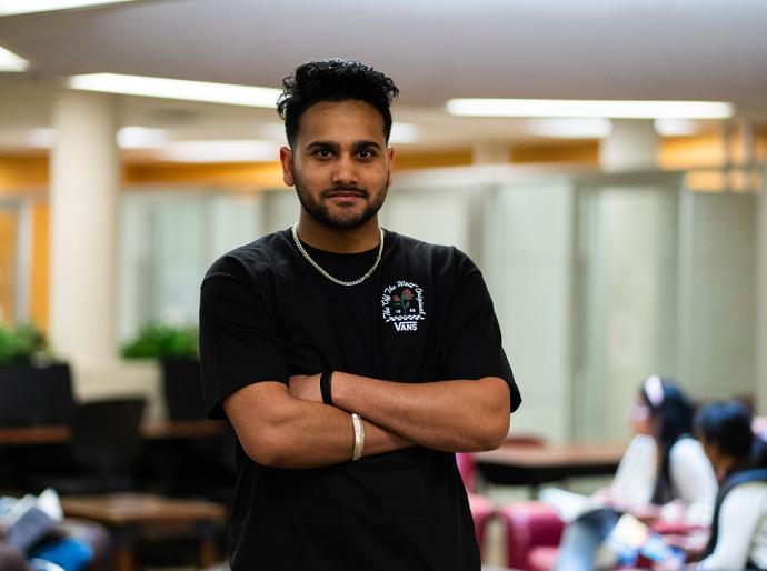 Happy student standing with arms folded in the library