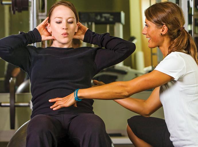 Kinesiologist observing and assisting a client who is working out with the correct exercise form