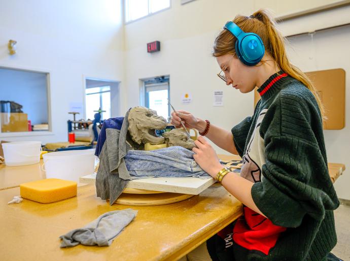 Arts student in the studio focused on creating a sculpture of a lion