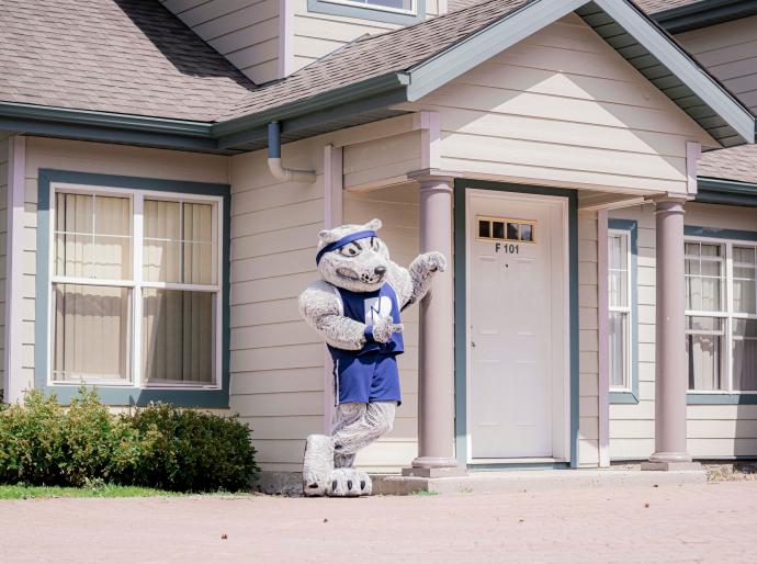 Farley, the Wolves mascot standing outside one of the on-campus residences on a sunny day
