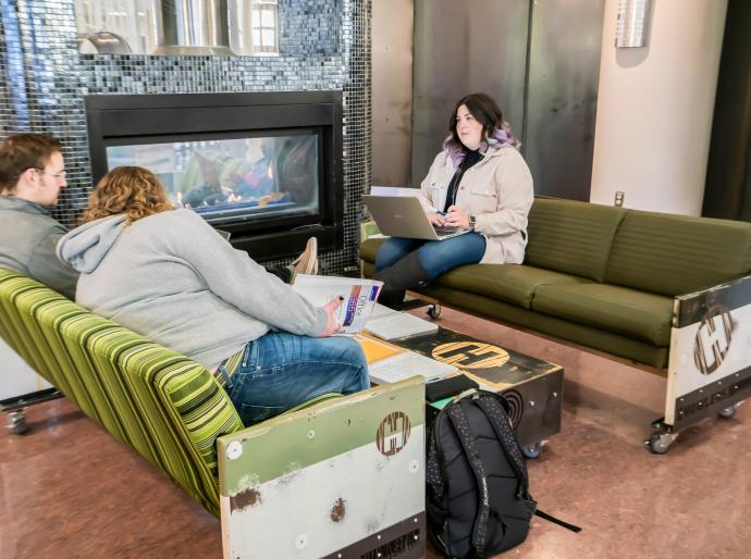 Three students sitting by the fireplace in Howlers lounge chatting and sharing notes