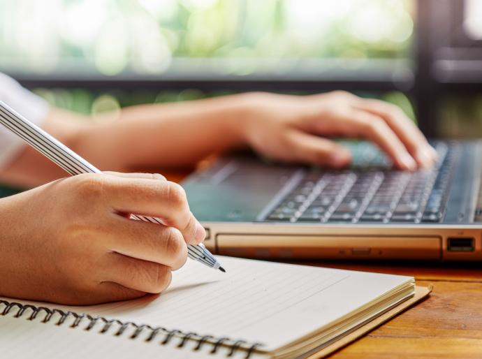 Student researching on a laptop while writing notes in a notebook