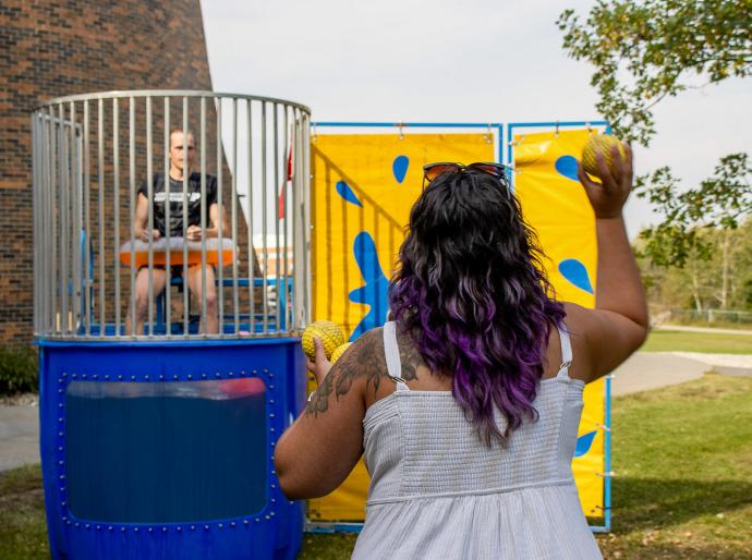 New student throwing a ball at a target on the dunk tank at orientation