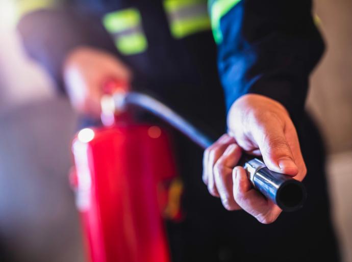A person holding the pipe of a fire extinguisher pointing at a fire