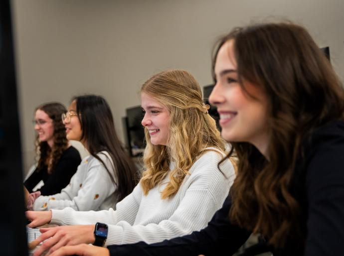 A group of students smiling and working on a project in the computer lab
