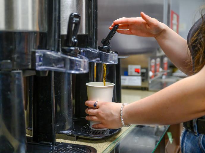 A student pours a cup of coffee from a flask in the cafeteria on Fairview campus