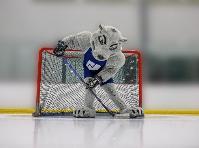 Wolves mascot, Farley on the ice holding a hockey stick with a puck in the foreground.