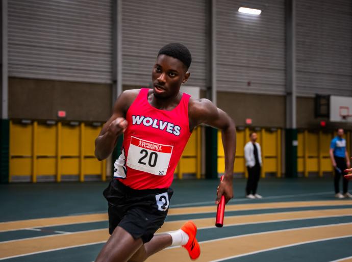 Men's wolves indoor track member running on track in race holding a baton