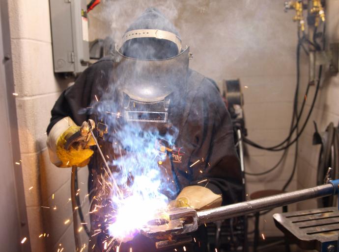 Welder working on a metal project with smoke and sparks flying