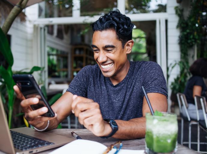 Young man sitting at a table in a café in front of his laptop and video chatting with a friend.