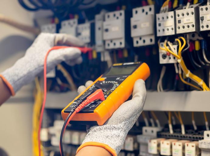 Electrician engineer uses a multimeter to test the electrical installation and power line current in an electrical system control cabinet.