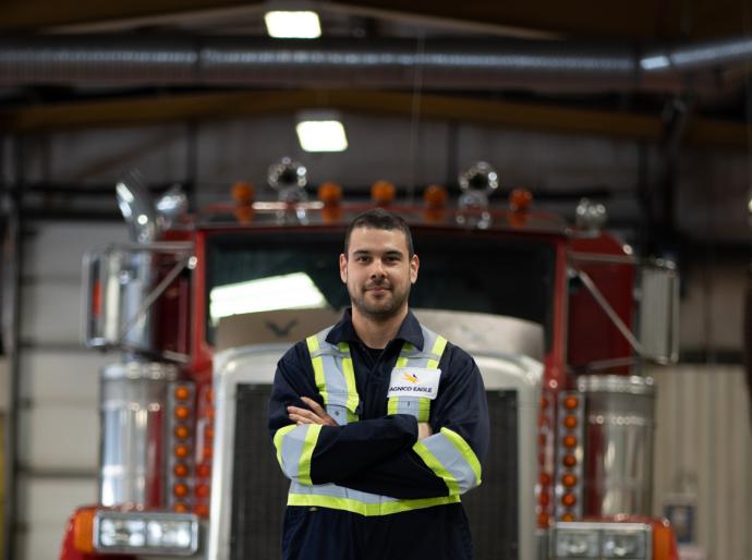 A heavy equipment technician standing with arms crossed in front of a semi truck