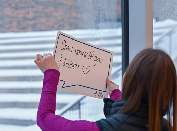 Student holding up a poster with a handwritten phrase inside a speech bubble that says "show yourself grace and kindness."