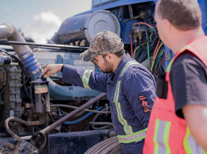 A driving instructor observes a student checking the engine of a semi-truck.