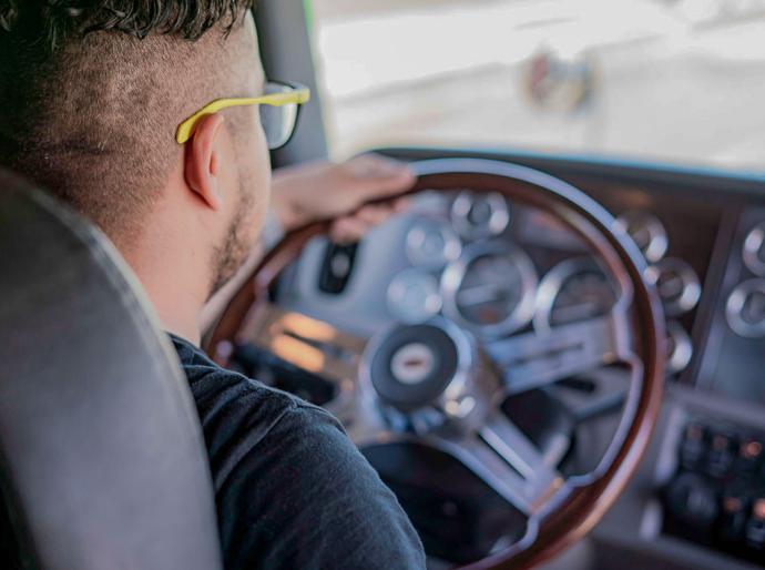 View from behind a truck driver with his hands on the steering wheel of a large semi truck