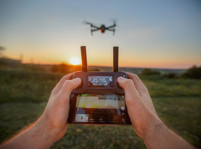 Close up of hands on a GPS remote control with a drone hovvering in the background.