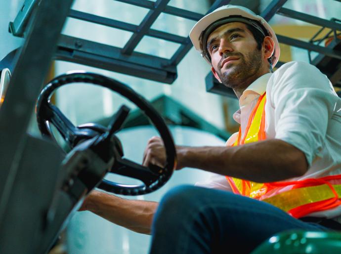 Forklift operator wearing a hi-vis vest and hard hat working in a warehouse