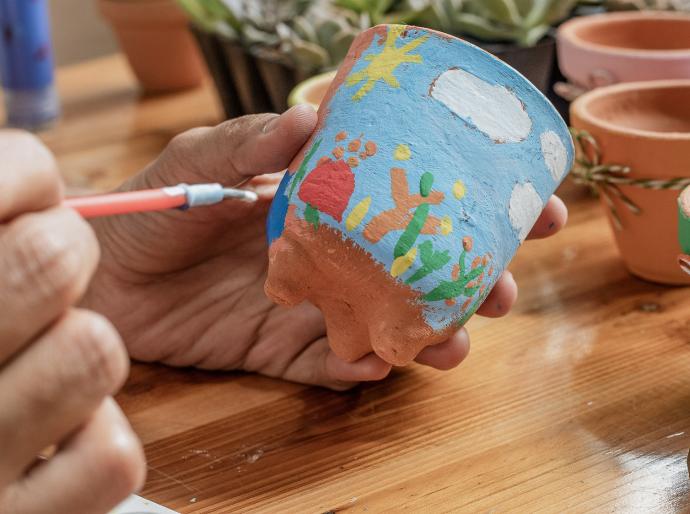 Close up shot of a person painting a colourful picture onto a clay pot