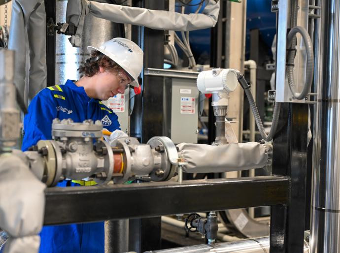 A power engineering studend wearing a hardhat and coveralls adjusts equipment in the power engineering lab