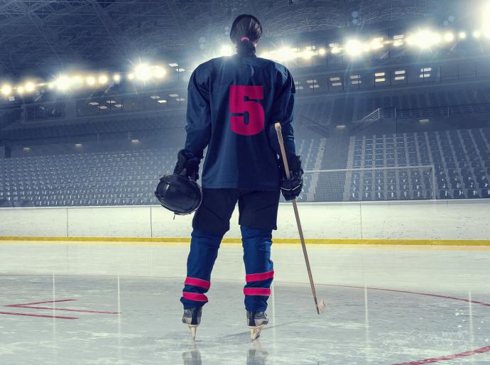 A female hockey player standing on the ice with her back to the camera displaying the number 5 on her jersey