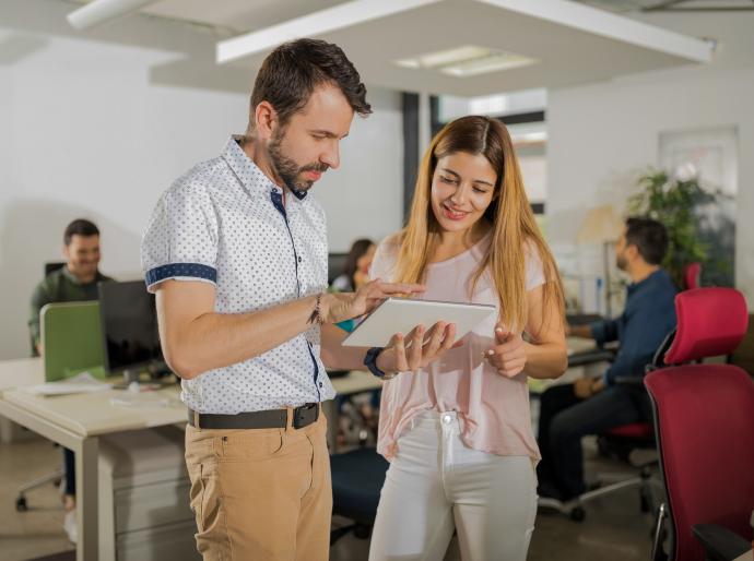 Supervisor assisting an employee in an open office with colleagues in the background
