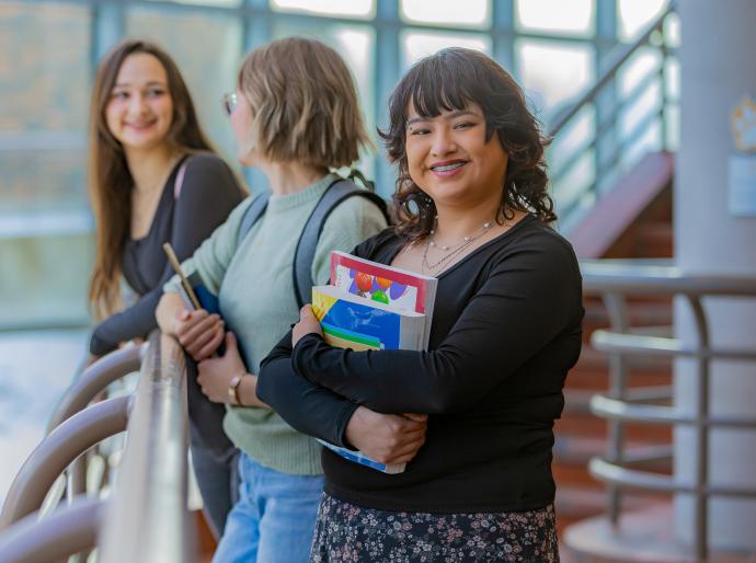 Happy student holding books and smiling as her friends socialize in the background