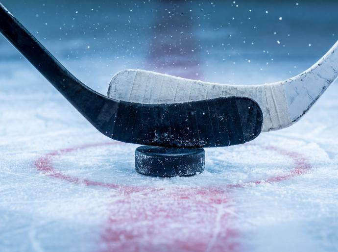 2 hockey sticks about to battle over a puck at centre ice