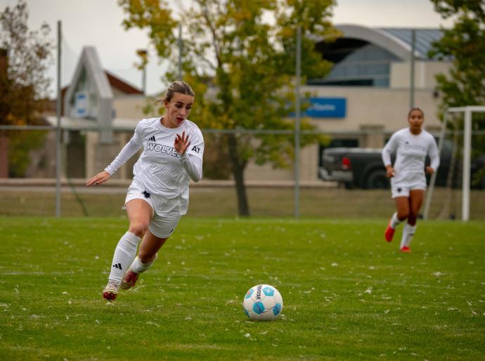Woles women's soccer player on the pitch dribbling the ball with a teammate behind her