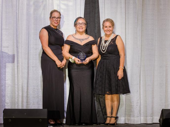 Board of Governors Award of Honour recipient Shannon Dunfield standing with her award on the stage at the President's Ball