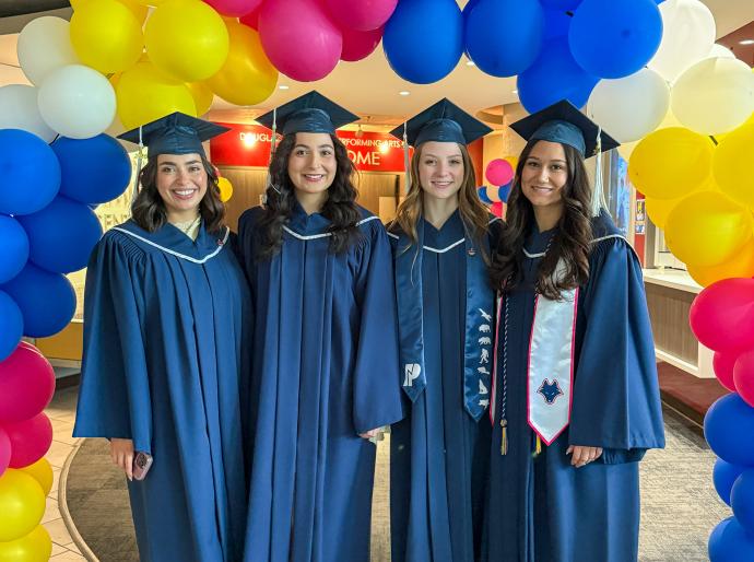 A happy group of graduates standing below a multicoloured balloon arch