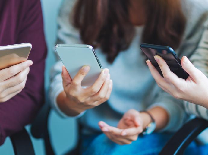 Group of young people using and looking at mobile phone while sitting together