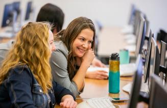 Student at a computer getting help from a staff member