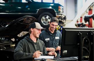 Automotive apprenticeship students interacting in a workshop with a vehicle in the background
