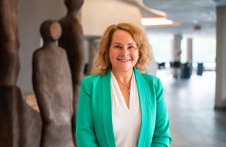 A cheerful Board of Governors Chair, Shawna Miller standing on the concourse of the Douglas J Cardinal Performing Arts Centre