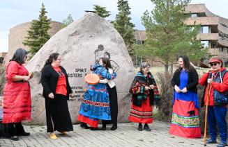Attendees embrace on Red Dress Day in front of the Spirt Sisters Rock on Grande Prairie Campus.